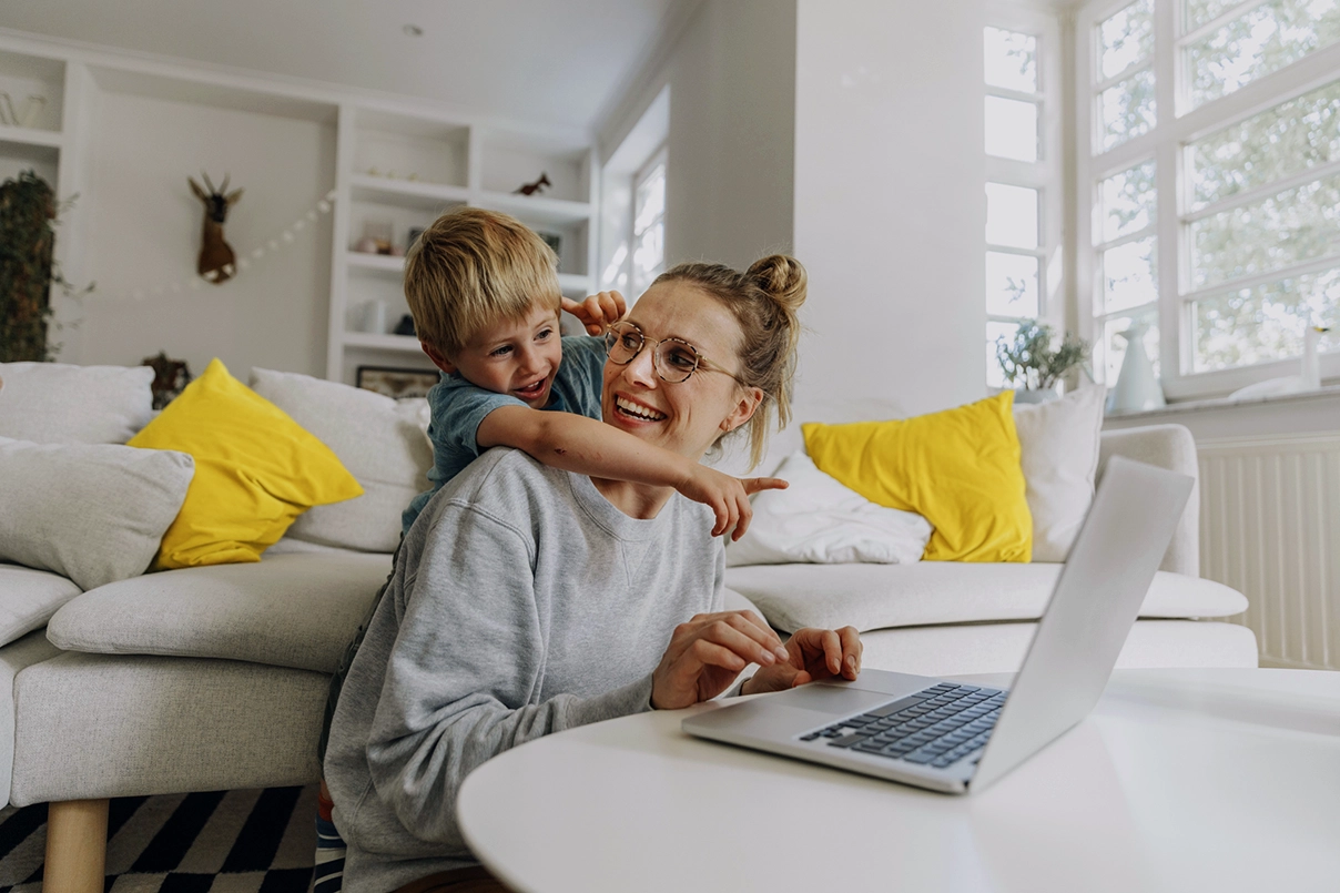 Eine Frau an einem Laptop mit einem Jungen, der hinter ihr steht und auf den Bildschirm zeigt. 